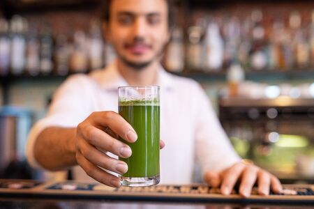 Hand of young barman holding glass of fresh vegetable smoothie over counterの写真素材