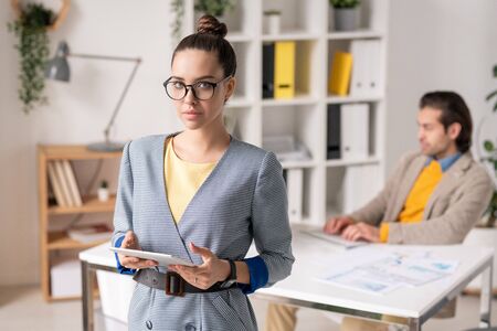 Young elegant businesswoman with tablet networking in front of camera