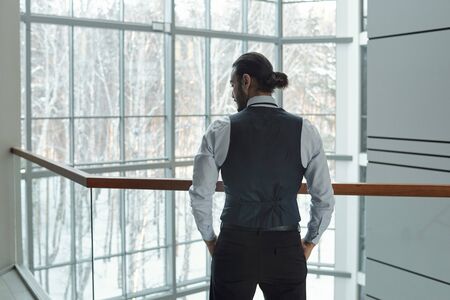 Rear view of young elegant businessman in formalwear keeping hands in pocketsの写真素材
