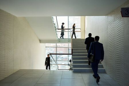 Large group of young contemporary office managers going upstairs and downstairs in the middle of...