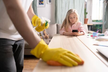 Young father in protective yellow rubber gloves sanitizing wooden tableの写真素材
