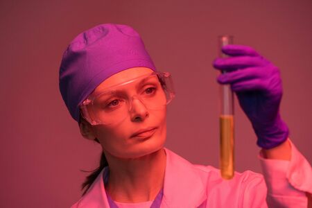 Young female laboratory worker looking at yellow liquid substance in flaskの写真素材