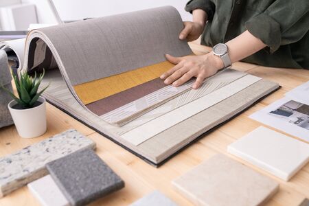 Hands of young designer of interior looking through samples of wallpapers