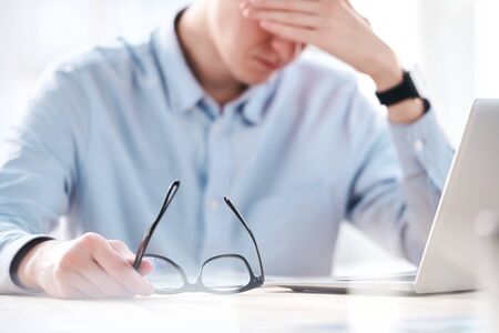 Close-up of puzzled businessman sitting in front of laptop and feeling migraine from exhaustion in...