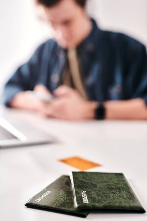 Man texting message while preparing for trip in background, focus on passports in green cases on...