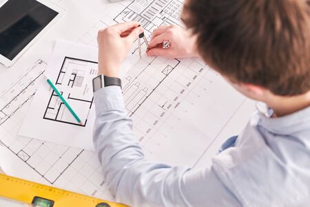 Above view of building engineer sitting at desk and using pair of compasses while working on floor...
