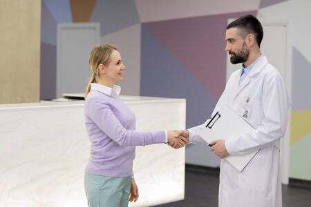 Pretty young blond woman in casualwear shaking hand of her doctorの写真素材