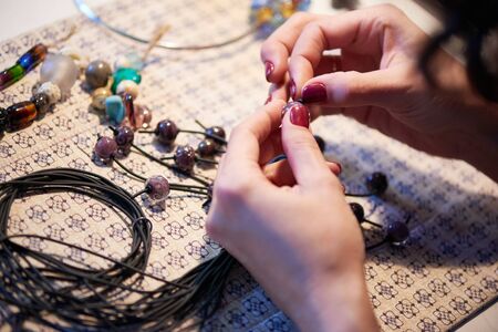 Hands of young craftswoman holding black plastic thread and glass beadの写真素材