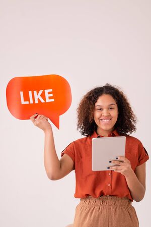 Portrait of smiling Afro-American girl with curly hair using digital tablet and liking post on social mediaの写真素材