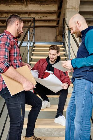 Group of young successful modern builders or architects discussing blueprint