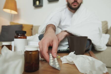 Hand of sick young man taking blister with painkillers or expectorantsの写真素材