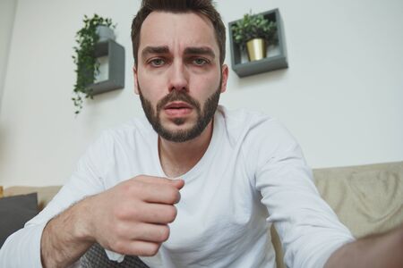 Young bearded man with covid19 or flu talking through video-chat at homeの写真素材