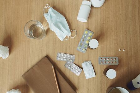 Wooden table with notebook, medical mask, tablets and pills, glass of waterの写真素材