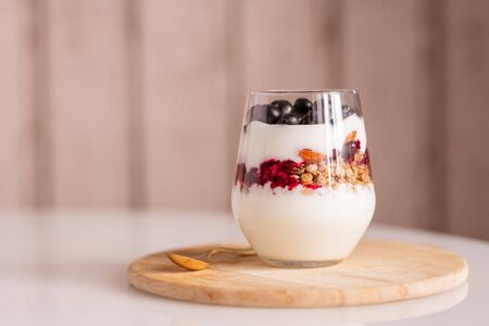 Glass with several layers of fresh yoghurt ingredients standing on wooden boardの写真素材