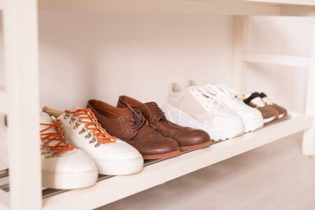 Row of sportive and casual footwear by wall on white lower shelf above the floorの写真素材