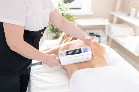 Unrecognizable massage therapist standing at procedure table and giving deep tissue massage to naked woman with lipomassage deviceの写真素材