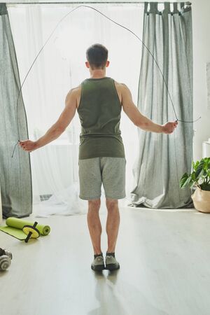 Rear view of young sportsman in activewear exercising with skipping-rope