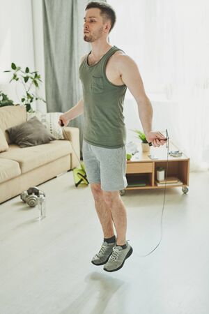 Contemporary young athlete jumping with skipping-rope in living-roomの写真素材