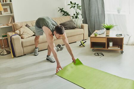 Contemporary sportsman putting mat on the floor while going to do yoga exercisesの写真素材