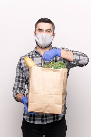 Male courier in protective mask and gloves delivering fresh food products to youの写真素材
