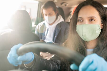 Serious female taxi driver in protective mask and gloves holding by steer