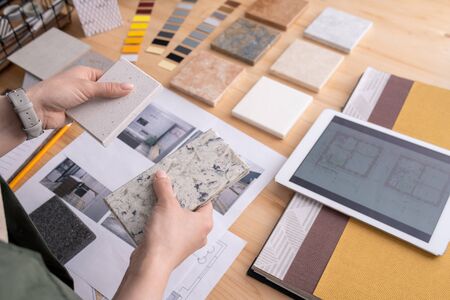 Hands of young female designer holding two samples of marble tile over wooden table with digital tablet, photos of home interior etcの写真素材