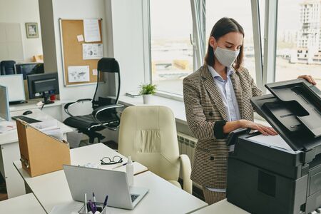 Young office woman in cloth mask scanning document in empty office during coronavirus epidemicの写真素材
