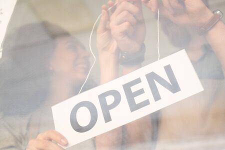 Hands of owners of cafe, restaurant or shop hanging notice announcing openの写真素材