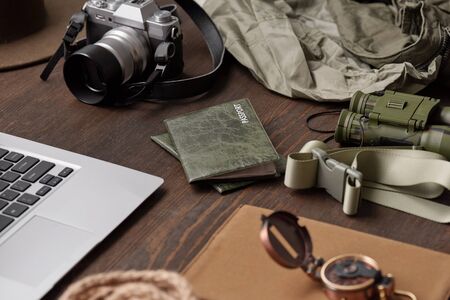 Close-up of passports in green covers, belt, binoculars, photographic camera, jackets and laptop on wooden tableの写真素材