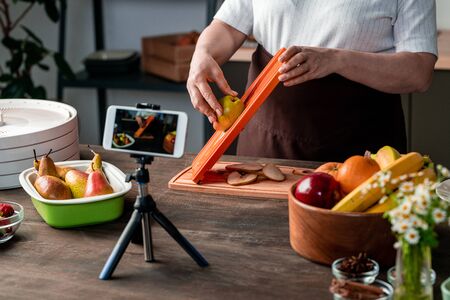 Housewife or blogger standing by kitchen table in front of smartphone cameraの写真素材