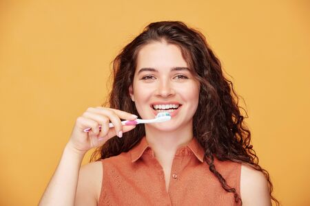Young laughing brunette woman with healthy smile brushing her teeth