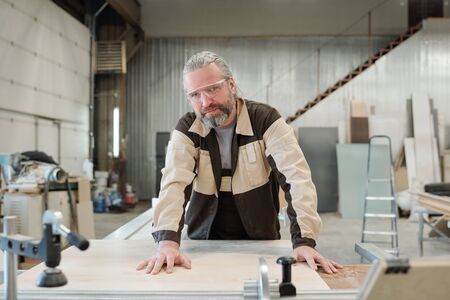 Aged male worker in workwear and protective eyeglasses looking at youの写真素材