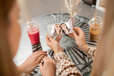 Hands of young female holding smartphone with selfie with her mother