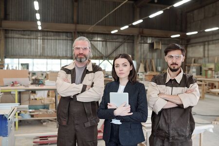 Young elegant manager with touchpad and two male workers in uniform