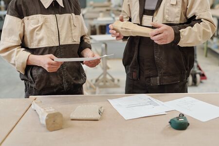 Mid section of two furniture factory workers in uniform standing by workbench