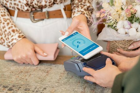 Hands of young female shopaholic holding smartphone over payment machineの写真素材