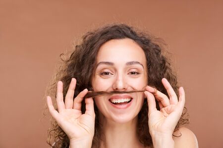 Joyful woman with toothy smile holding bunch of hair between her mouth and noseの写真素材