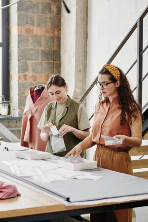 Two young female tailors in casualwear packing new shoulder pads for coats