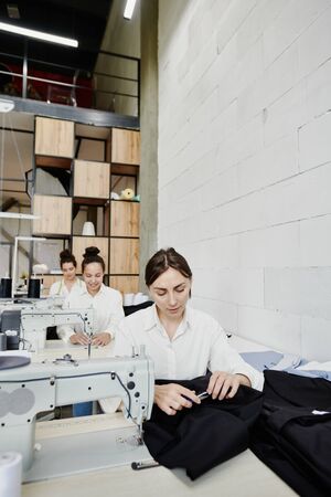 Three young seamstresses sitting in row by electric sewing machinesの写真素材