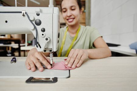 Hands of happy young tailor by electric sewing machine making shoulder padsの写真素材