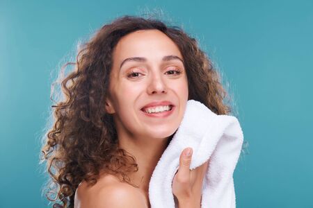Cheerful woman with healthy skin drying her face with white soft cotton towelの写真素材