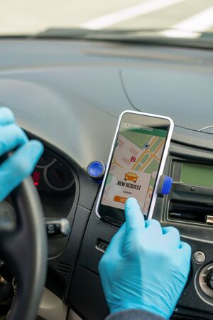 Close-up of unrecognizable taxi driver in latex gloves pushing button on touchscreen while starting...