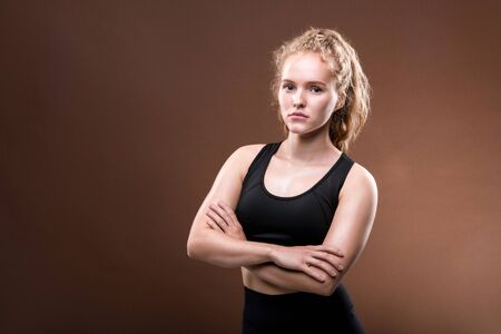 Serious young fit female with long blond curly hair crossing her arms on chest