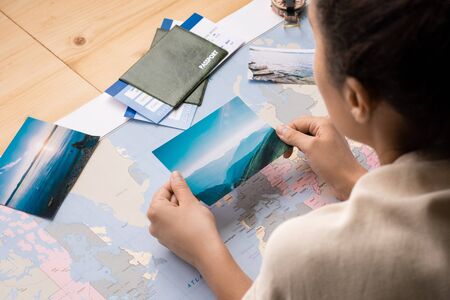 Over shoulder view of woman leaning on table with world map and watching photos while dreaming of...