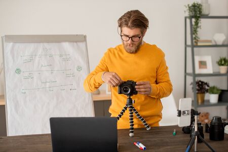 Young photographer or teacher of photography showing professional photocamera