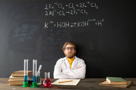 Young contemporary chemistry teacher in whitecoat crossing his arms on chest
