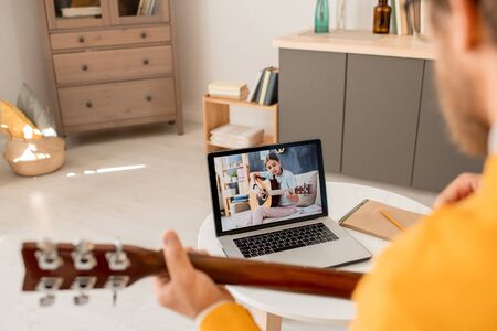 Laptop display with diligent teenage girl playing guitar while sitting on couchの写真素材