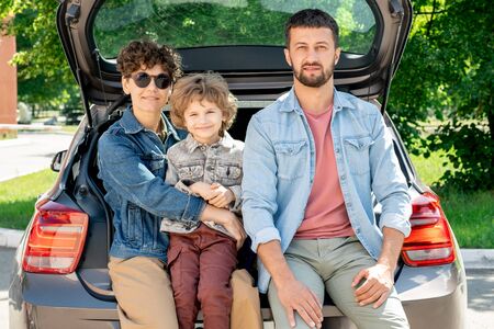 Young affectionate family of father, mother and son sitting in the car trunk