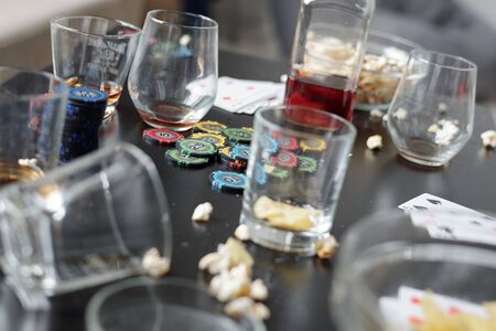 Close-up of empty dirty glasses, poker chips, playing cards and popcorn on table after poker partyの写真素材