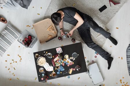 Above view of young man lying on floor and watching party photos after home partyの写真素材